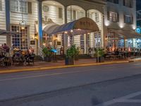 an outdoor restaurant on the side of the road in front of a white building at night