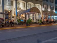 an outdoor restaurant on the side of the road in front of a white building at night