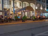 an outdoor restaurant on the side of the road in front of a white building at night