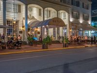 an outdoor restaurant on the side of the road in front of a white building at night