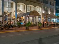 an outdoor restaurant on the side of the road in front of a white building at night