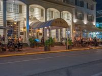 an outdoor restaurant on the side of the road in front of a white building at night