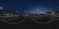 some empty cars parked in the parking lot at night time with city lights overhead and buildings to the right