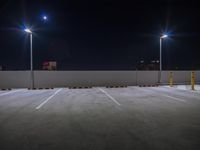 empty parking lot lit up by three streetlights and lights at night with city skyline in distance