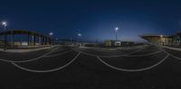 some empty cars parked in the parking lot at night time with city lights overhead and buildings to the right