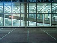 a parking lot near large windows is shown at night time, and has no cars