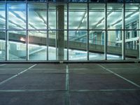 a parking lot near large windows is shown at night time, and has no cars