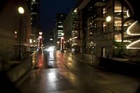 the street is wet at night with the traffic passing through it and lights on the buildings behind