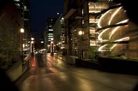 the street is wet at night with the traffic passing through it and lights on the buildings behind
