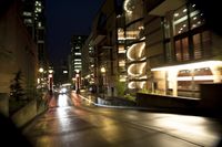 the street is wet at night with the traffic passing through it and lights on the buildings behind