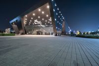 a black tiled walkway with the lights on and in front of an opera building lit up