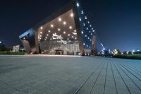 a black tiled walkway with the lights on and in front of an opera building lit up