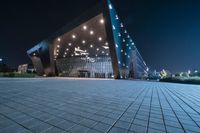 a black tiled walkway with the lights on and in front of an opera building lit up