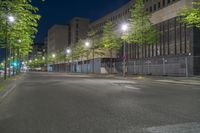 the empty road in the middle of a city at night with green trees near by