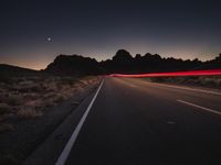 a road with light trails along the side and hills in the distance as part of a long exposure camera