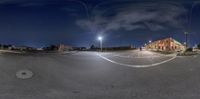 an empty parking lot that is near some stores at night time with lights on the buildings and sky in the background