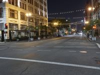 an intersection with many lights hanging on the buildings at night, with people standing on the sidewalk