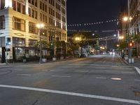 an intersection with many lights hanging on the buildings at night, with people standing on the sidewalk