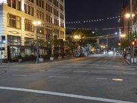 an intersection with many lights hanging on the buildings at night, with people standing on the sidewalk