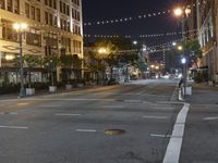 an intersection with many lights hanging on the buildings at night, with people standing on the sidewalk