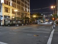 an intersection with many lights hanging on the buildings at night, with people standing on the sidewalk