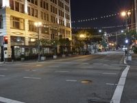 an intersection with many lights hanging on the buildings at night, with people standing on the sidewalk