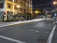 an intersection with many lights hanging on the buildings at night, with people standing on the sidewalk