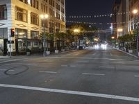 an intersection with many lights hanging on the buildings at night, with people standing on the sidewalk