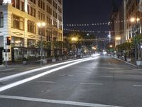 an intersection with many lights hanging on the buildings at night, with people standing on the sidewalk