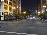 an intersection with many lights hanging on the buildings at night, with people standing on the sidewalk