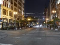 an intersection with many lights hanging on the buildings at night, with people standing on the sidewalk