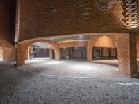 brick structures surround two circular space in a building with arches in the foreground, and cobblestone walkway around them