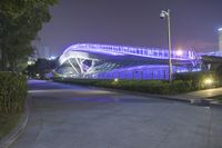 there is a large modern building on this side of the street at night, with a person walking by