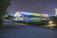 there is a large modern building on this side of the street at night, with a person walking by