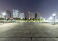 a person sitting on a skate board in an empty parking lot at night time with street lights and buildings around