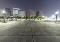 a person sitting on a skate board in an empty parking lot at night time with street lights and buildings around