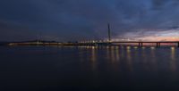 a lighted up bridge over the ocean in the twilight sun sets behind it and lights up on other bridges