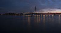 a lighted up bridge over the ocean in the twilight sun sets behind it and lights up on other bridges