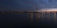 a lighted up bridge over the ocean in the twilight sun sets behind it and lights up on other bridges