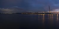 a lighted up bridge over the ocean in the twilight sun sets behind it and lights up on other bridges