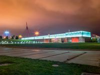 a nighttime shot of a lighted building near an empty parking lot with lights on it