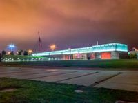 a nighttime shot of a lighted building near an empty parking lot with lights on it