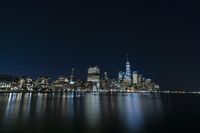 a photo with several very tall buildings near some water and the lights are on and buildings in the background