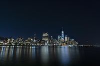 a photo with several very tall buildings near some water and the lights are on and buildings in the background