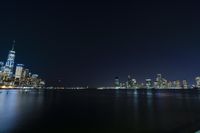 a photo with several very tall buildings near some water and the lights are on and buildings in the background