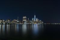 a photo with several very tall buildings near some water and the lights are on and buildings in the background