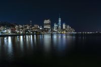 a photo with several very tall buildings near some water and the lights are on and buildings in the background