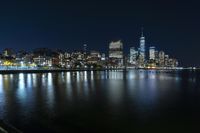 a photo with several very tall buildings near some water and the lights are on and buildings in the background