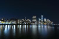 a photo with several very tall buildings near some water and the lights are on and buildings in the background