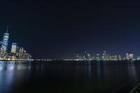 a photo with several very tall buildings near some water and the lights are on and buildings in the background